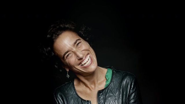 Close up of a cheerful woman with short hair isolated on black background. Happy senior woman looking at camera and laughing.
