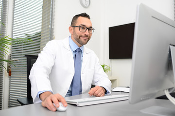 Fototapeta premium man male doctor professor scientist teacher in medical office at desk with computer wearing white lab coat research covid19 and coronavirus