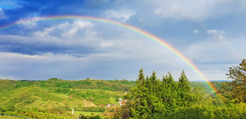 Spring rural rainbow landscape, view of green meadows and hills