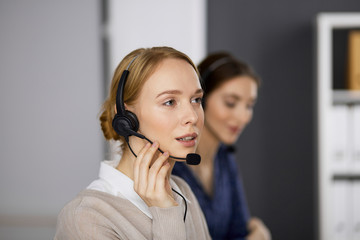 Friendly businesswoman talking by headset in office. Call center and diverse people group in...
