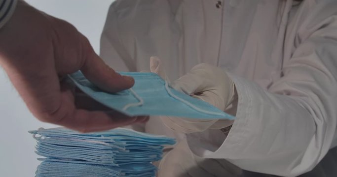 Unrecognizable volunteer or doctor in white medical robe and protective gloves giving face masks to unknown people. Global Covid-19 pandemic, protection, volunteering. Cinema 4k ProRes HQ.