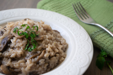Classic Italian vegan mushroom risotto made with arborio rice, mushrooms, onion and garlic garnished with basil ribbons on a rustic wooden surface with a green napkin and a fork