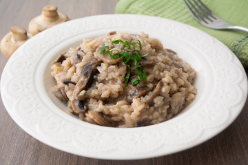 Classic Italian vegan mushroom risotto made with arborio rice, mushrooms, onion and garlic garnished with basil ribbons on a rustic wooden surface with a green napkin and a fork