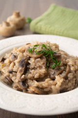 Classic Italian vegan mushroom risotto made with arborio rice, mushrooms, onion and garlic garnished with basil ribbons on a rustic wooden surface with a green napkin and a fork