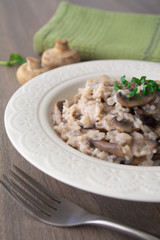 Classic Italian vegan mushroom risotto made with arborio rice, mushrooms, onion and garlic garnished with basil ribbons on a rustic wooden surface with a green napkin and a fork