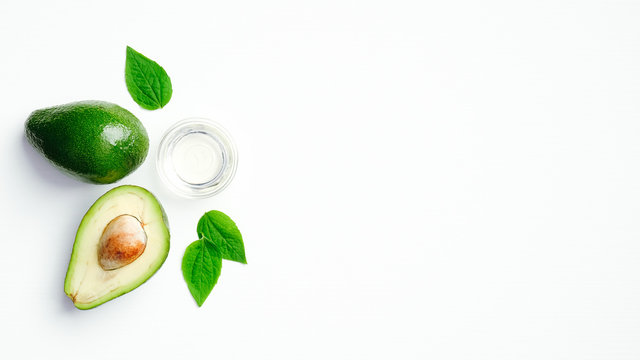 Fresh ripe avocado and bowl with essential oil on white background. Flat lay, top view. Healthy cooking or organic cosmetic ingredients concept.
