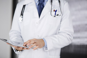 Male doctor using tablet computer in clinic, close-up. Perfect medical service in hospital. Medicine and healthcare concept