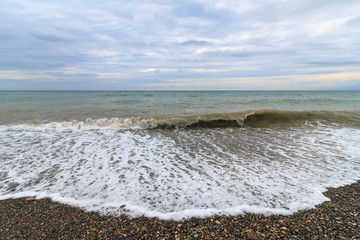 Stormy wave on a pebble beach in Batumi. Cloudy sky before sunset. Nature concept, design for postcard or calendar. Adjara Autonomous Republic (Adjaria), Georgia. Sea evening landscape.