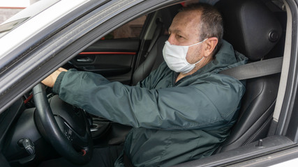 Portrait of man driving a car wearing a hygienic mask to prevent airborne respiratory diseases such as infection, influenza and coronavirus (COVID-19).
