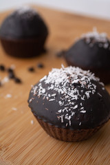 Chocolate glazed chocolate cocoa crazy cake muffins with coconut flakes on a wooden board with coconut flakes and chocolate chips sprinkled on it