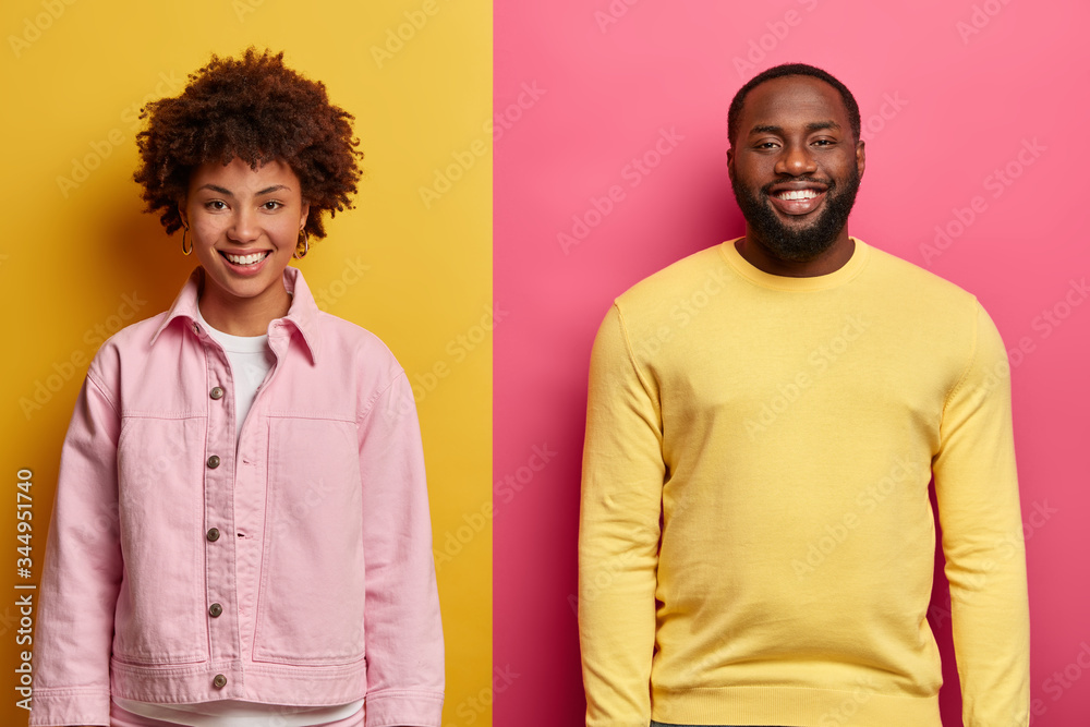 Poster Horizontal shot of happy African American woman and man smile satisfied, stand next to each other against two colored background, glad to hear excellent news from interlocutor, work as team.