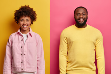 Horizontal shot of happy African American woman and man smile satisfied, stand next to each other...