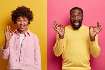 Positive dark skinned smiling woman and man show okay gestures with satisfied assertive...