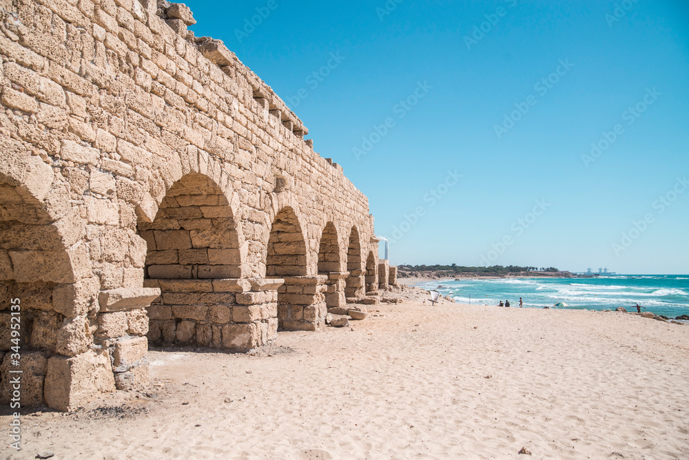 Wall mural ancient roman aquaduct leading to bright blue ocean