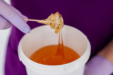 Women beautician holds jar wax of paste for sugar depilation shugaring, white background.