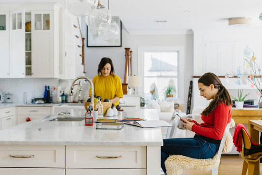Teen Girl Texting on Smartphone at home in Kitchen with Mother