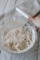 Hand covering with plastic wrap a bowl with bread dough