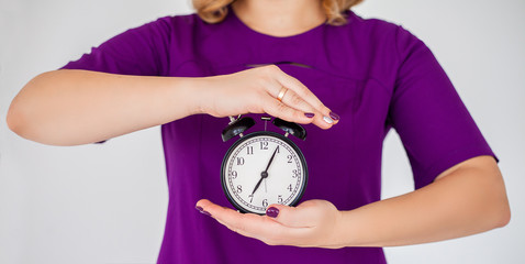 Woman in purple uniform holding alarm clock in hand on grey background isolation.
