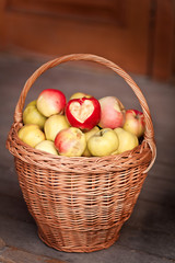 A wicker basket with red and yellow apples. Apple with a heart. Autumn garden. Gift of nature. Crop of apples. Organic gardening.