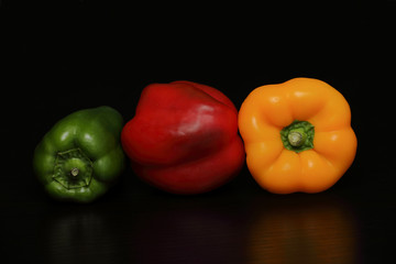 Still life with three peppers of red, yellow and green colors on a black background