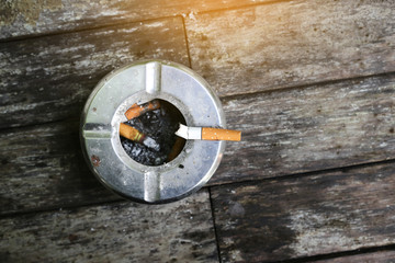Metal ashtray with cigarette on wood table