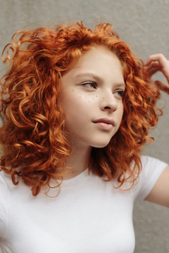 The portrait of the curly red hair girl with heart shaped fake freckles staying near the wall on the street
