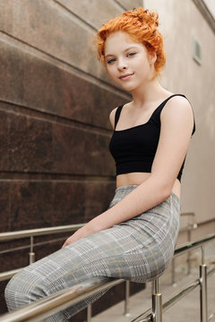 The red head curly girl sitting on the handrail on the street