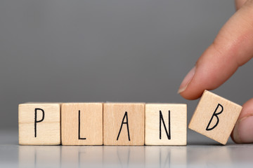 Wooden cubes with the word Plan B on grey background and human finger, business concept background