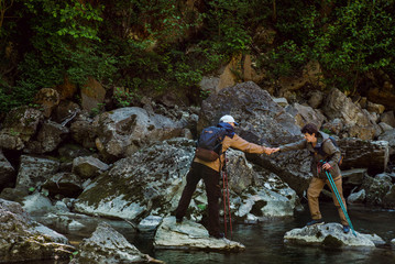 A man helps a woman to cross the mountain river during a hiking trip
