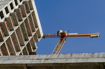 Concrete building under construction and a yellow tower crane against the blue sky.