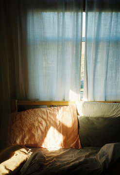 Pillows on a messy bed with light linen stroked by the morning sunlight