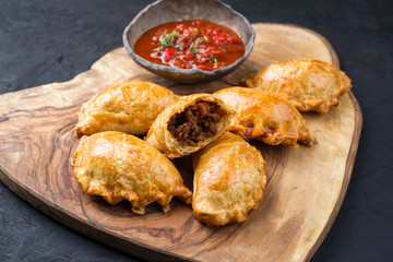 Traditional South American empanada de carne offered with a chili dip as closeup on a rustic wooden board