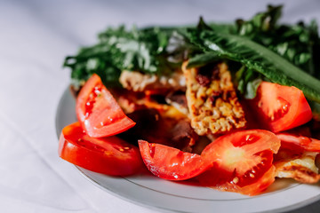 Traditional indonesian culinary food. Fried tempe in soy sauce, on red and black pepper. Greens and vegetables on a white plate. Beautiful sunlight is falling from the window.