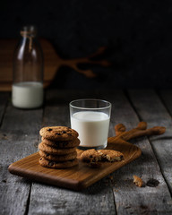 A glass of milk with oatmeal cookies on a blackboard on a table made of old wooden boards.