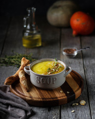 Pumpkin cream soup in a bowl with nuts and thyme on a wooden stand with bread sticks.