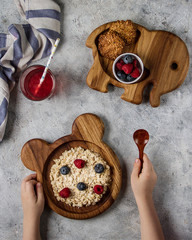 Children's wooden plates in the form of animals, bear and elephant. The child eats porridge with berries, cookies and juice.