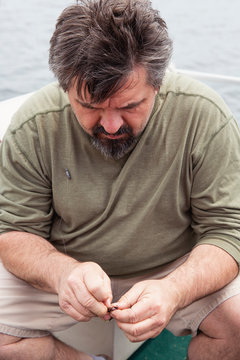 Portrait of an older man with peppered hair and a goatee baiting his hook in preparation for fishing
