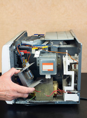 Repair of a microwave oven, repair of household appliances. Engineer removes air duct with a light bulb