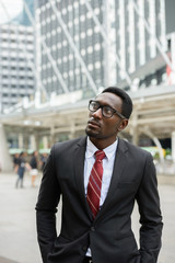 Young handsome African businessman thinking in front of modern building at Bangkok city