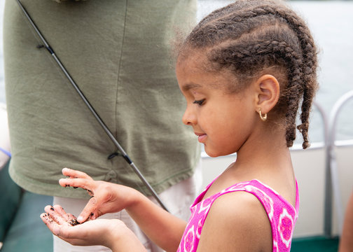 Cute Young Girl With Cornrow Braids Examining The Bait Worms While On The Boat During A Fishing Trip