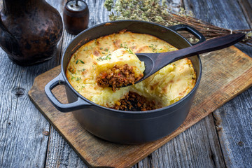 Traditional English shepherd pie offered as closeup in a Dutch oven on a wooden board