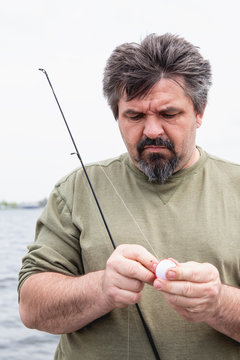 Portrait of an older man with peppered hair and a goatee baiting his hook in preparation for fishing