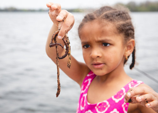 Cute young girl with cornrow braids examining the bait worms while on the boat during a fishing trip