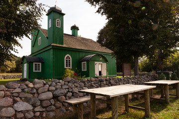 Green wooden building (mosque) and picnic tables in front foreground. Stone fence around. Kruszyniany, Poland, Europe.
