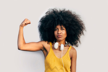 Afro woman looking at camera besides a grey wall