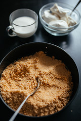 A baking tray with crushed crackers stands on a black table