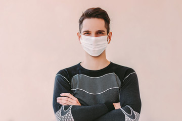 Portrait confident sports man in medical face mask keeping arms crossed and smiling against...
