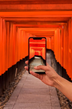 Tourist taking a picture of orange wooden pillars in Kyoto, Japan