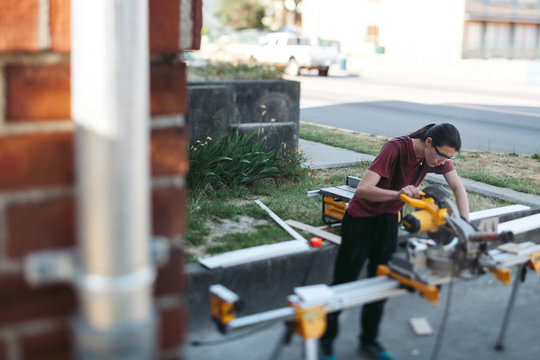 Young Woman Using Chop Saw To Cut Baseboard Trim