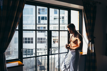 Sexy adult man enjoying the sun rays standing besides the window